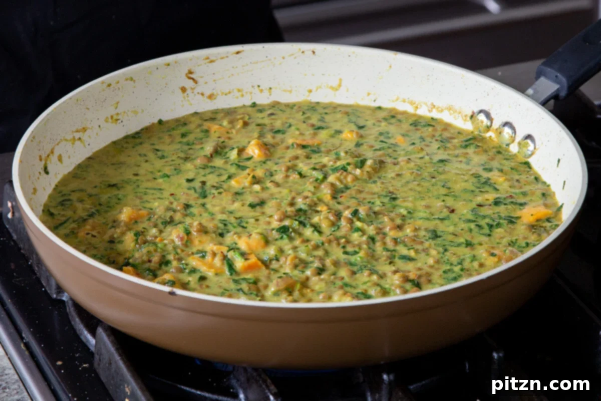 The finished lentil coconut curry simmering gently in the frying pan on the stovetop, garnished and ready to serve.
