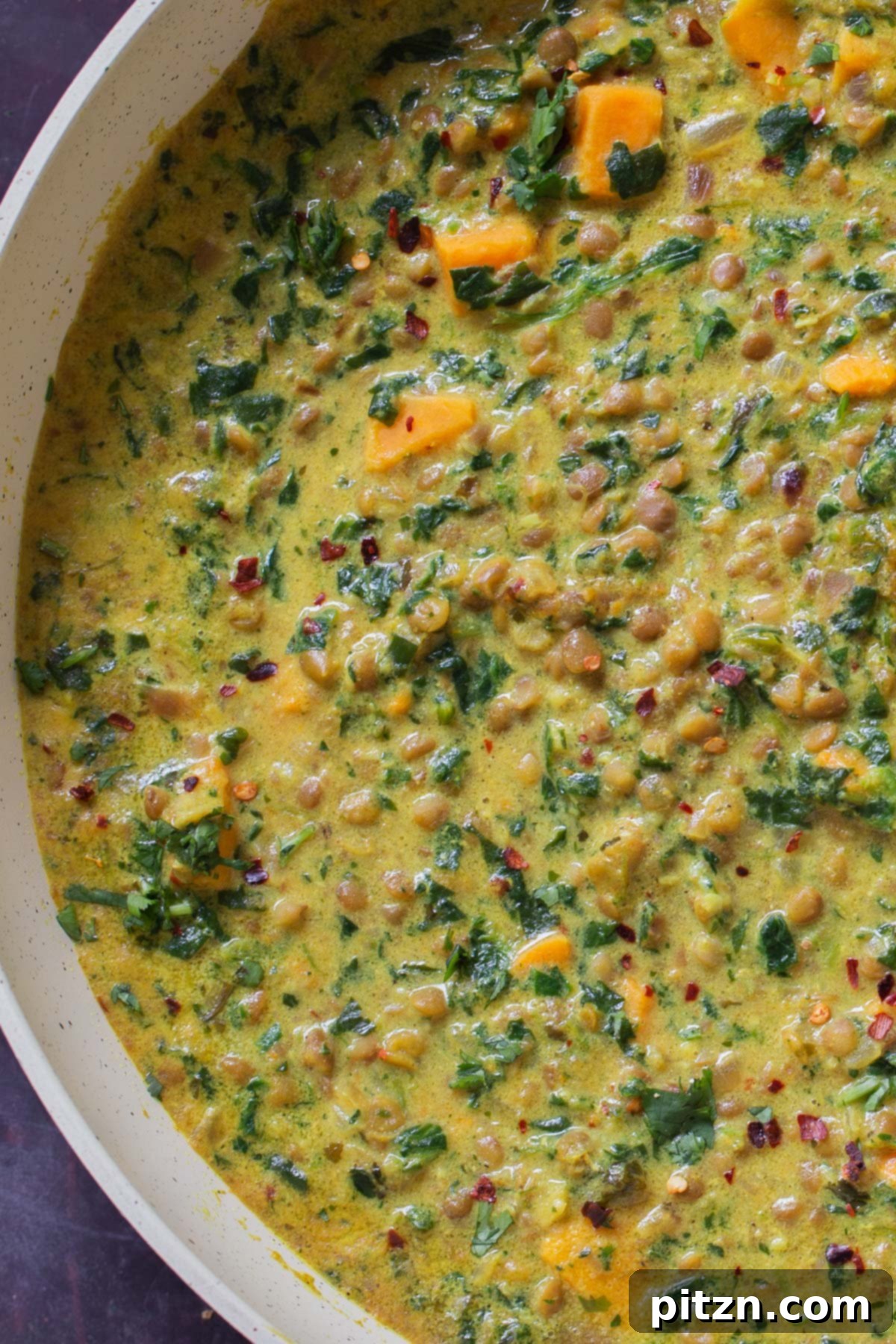 A close-up shot of the simmering lentil coconut curry in a pan, highlighting its rich texture and ingredients.