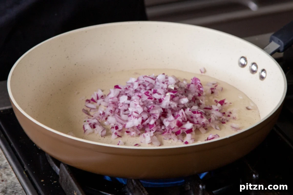 Adding chopped onion to a hot pan with oil, beginning the sautéing process for the curry base.