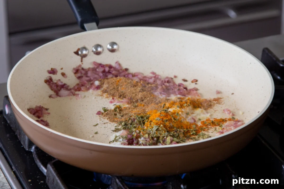 Sprinkling dried spices, including turmeric and garam masala, over the onion and ginger-garlic mixture in the pan.