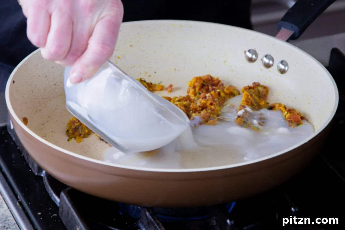 Adding creamy coconut milk to the spiced onion mixture in the pan, forming the rich base of the curry.