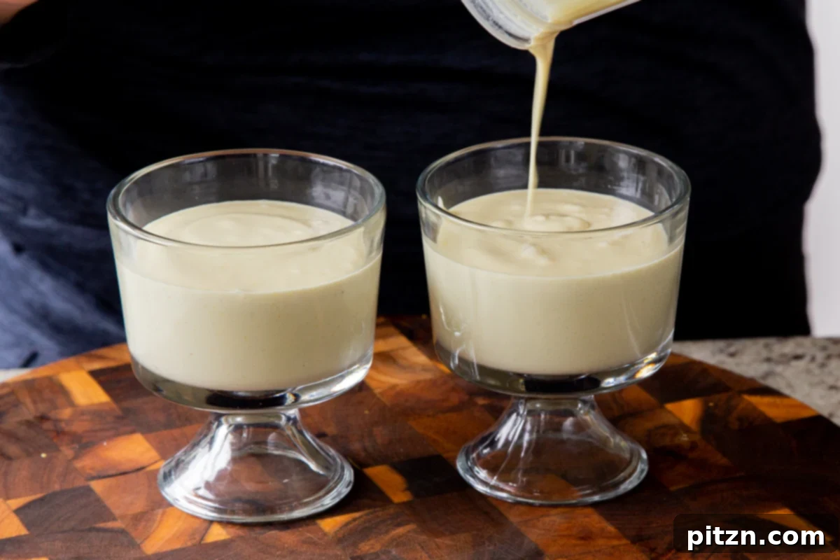A close-up shot of the creamy lemon pudding mixture being poured from a blender into small glass cups.