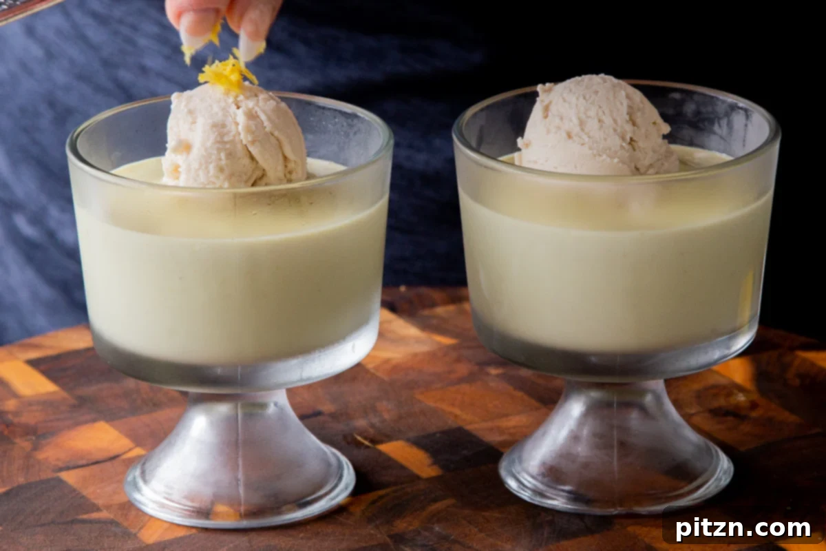 Hands adding fresh lemon zest to a scoop of vanilla ice cream atop a cup of vegan lemon pudding.