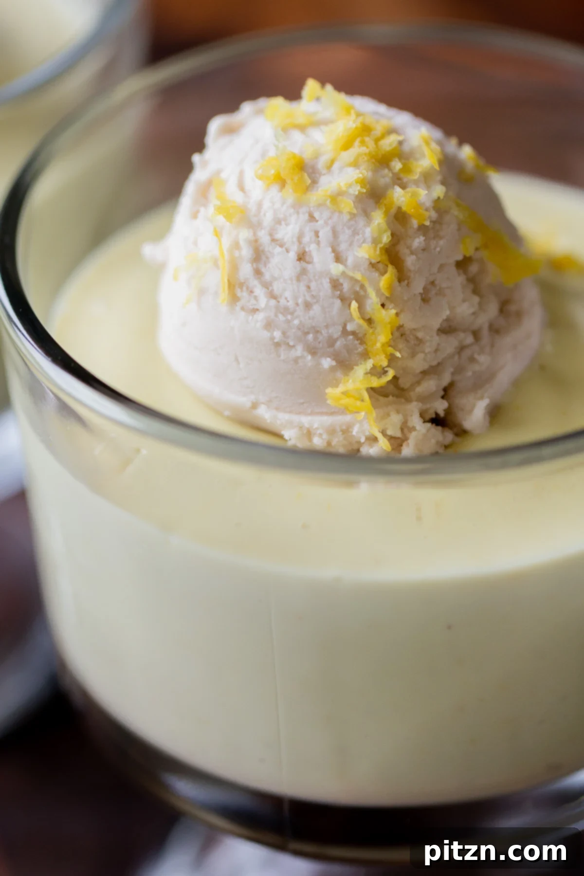 Close-up shot of a single cup of creamy vegan lemon pudding, generously topped with a scoop of white vegan vanilla ice cream and delicate lemon zest curls.