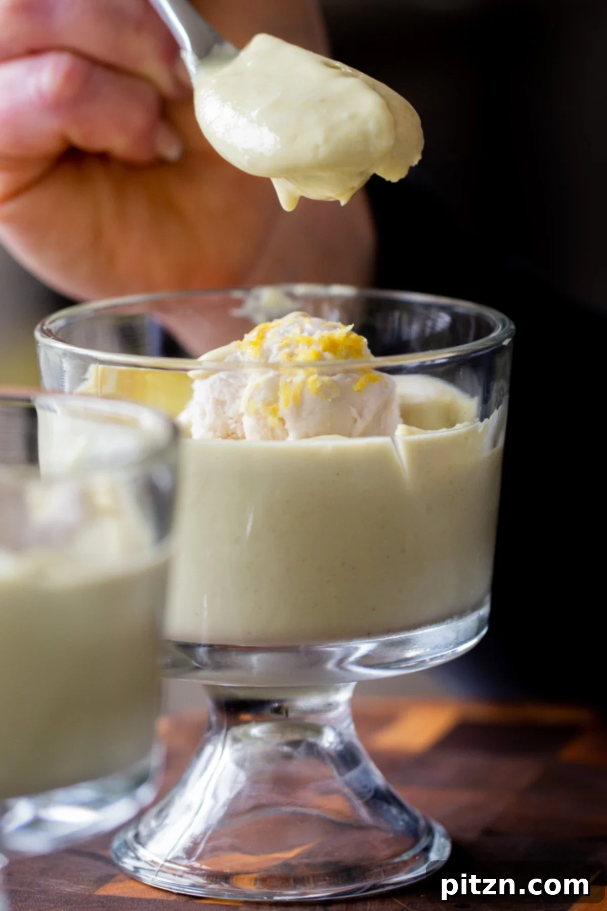 A spoon diving into a cup of vegan lemon pudding, showing its thick and creamy texture.
