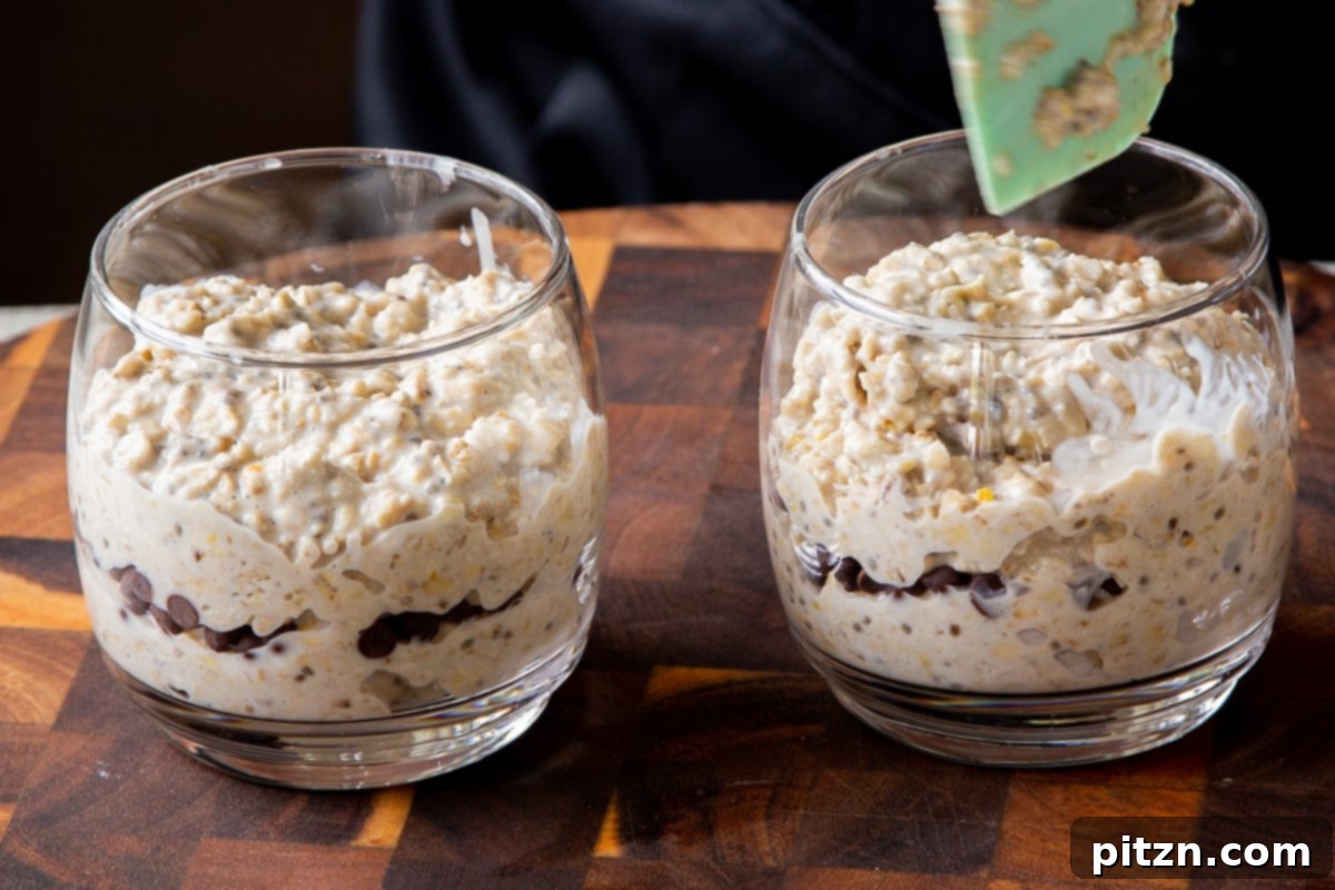 Easy Cannoli Overnight Oats: 30-Minute, Gluten-Free & Soy-Free 15 Two glass cups showcasing layered overnight oats, with creamy oat mixture at the bottom, a visible layer of chocolate chips in the middle, and more oats on top.