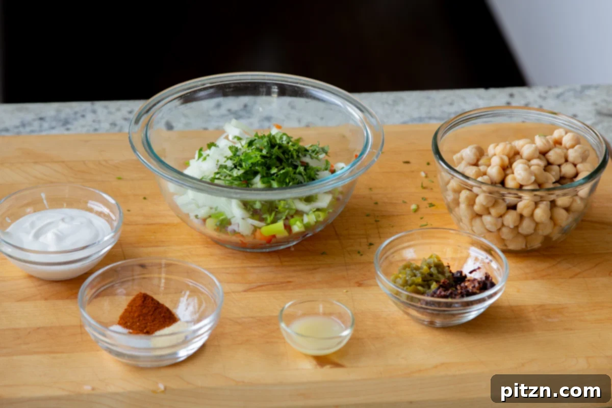 chickpeas, veggies, and other salad ingredients in bowls on a wooden cutting board