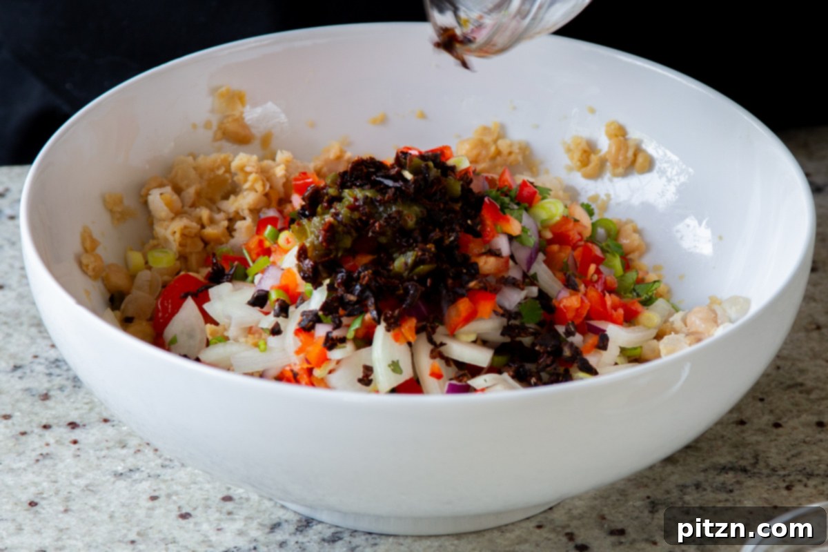 adding sun-dried tomatoes and spices to the bowl of mashed chickpeas and veggies
