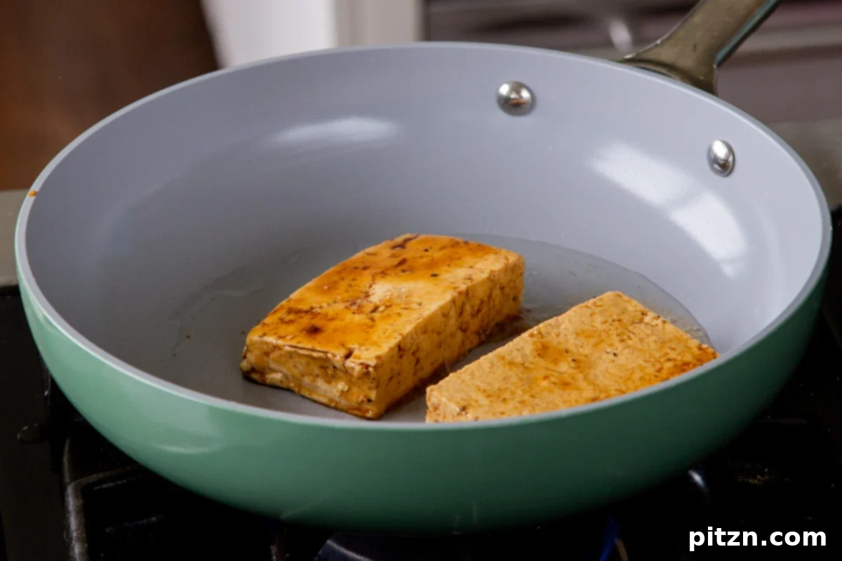 Carefully placing marinated tofu slabs into a hot frying pan with a small amount of oil, ready for searing until golden and caramelized.