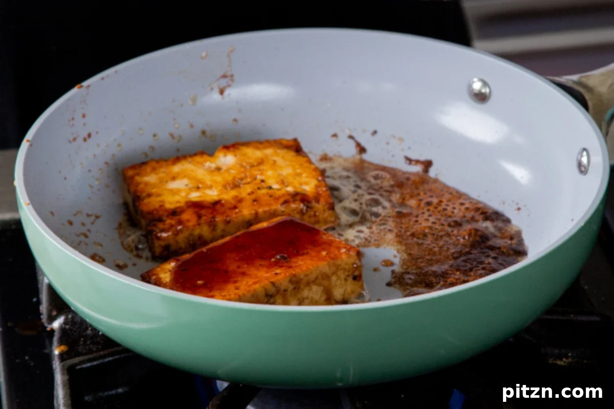 Tofu slabs searing in the pan, showing a rich golden-brown color developing on the cooked side, indicating caramelization.