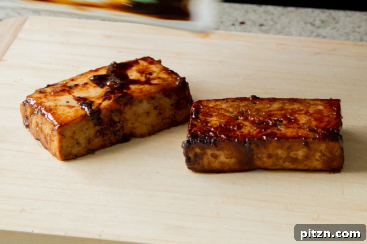 Perfectly seared tofu resting on a cutting board, displaying its golden-brown exterior and glaze, before being sliced into topping pieces.