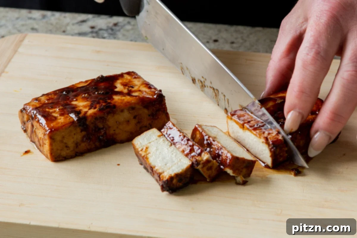 A knife expertly slicing through a seared tofu slab on a cutting board, creating even, appetizing pieces for topping the ramen.