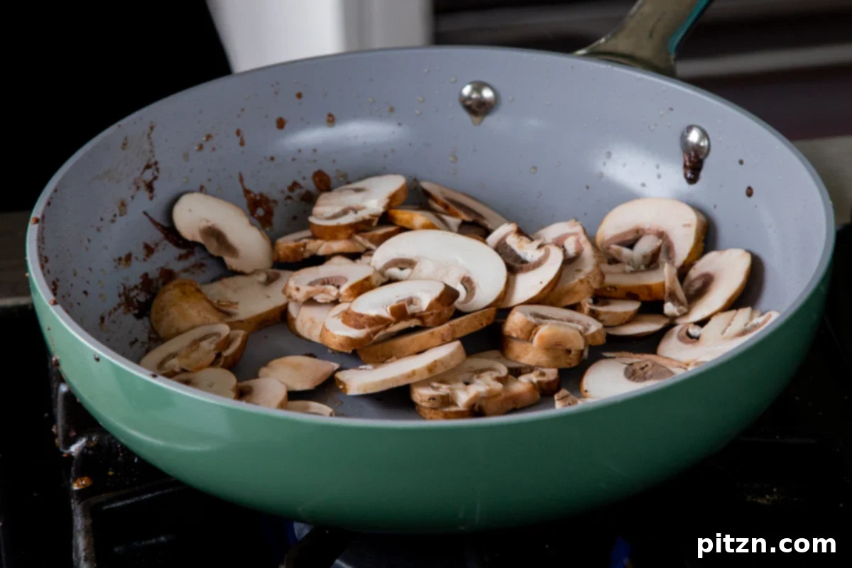 Sliced mushrooms being added to a hot frying pan with oil, ready to be sautéed until golden and tender for the ramen broth base.