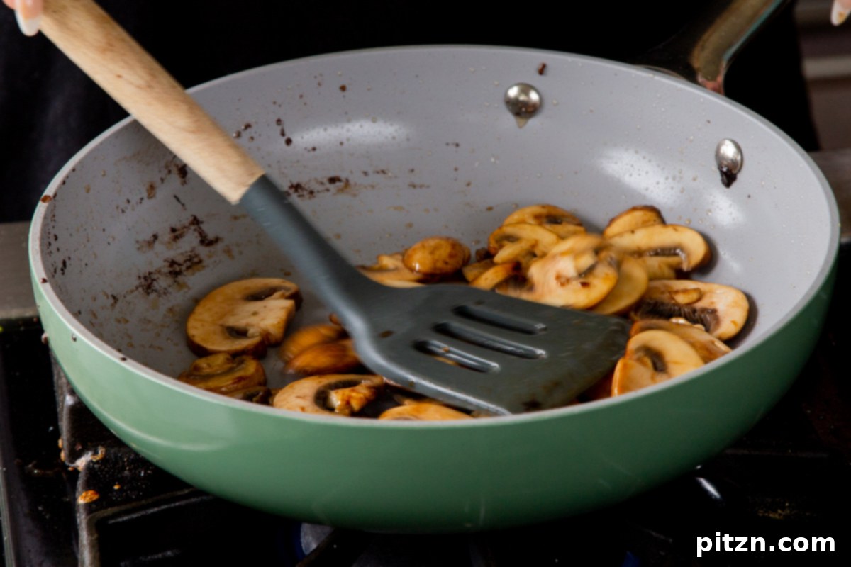 Sautéed mushrooms in the frying pan, now golden brown and tender, indicating they are ready for the next step of building the broth.