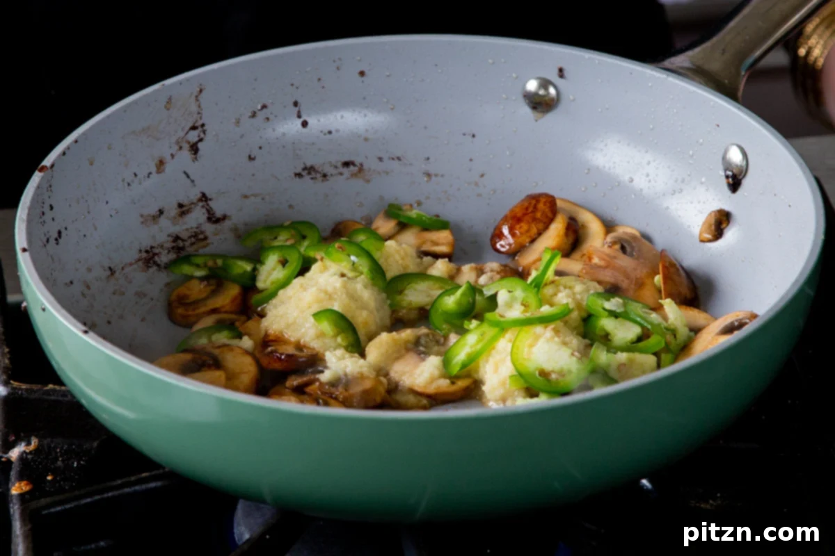 Adding ginger-garlic paste and thinly sliced jalapeños to the sautéed mushrooms in the frying pan, for an aromatic broth base.