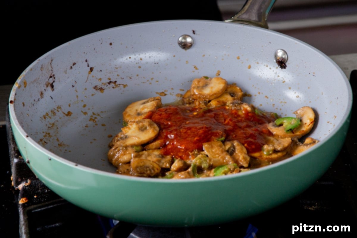 Sautéed mushrooms and vibrant sambal oelek mixed in the frying pan, showing the rich color of the chili paste integrated into the aromatics.
