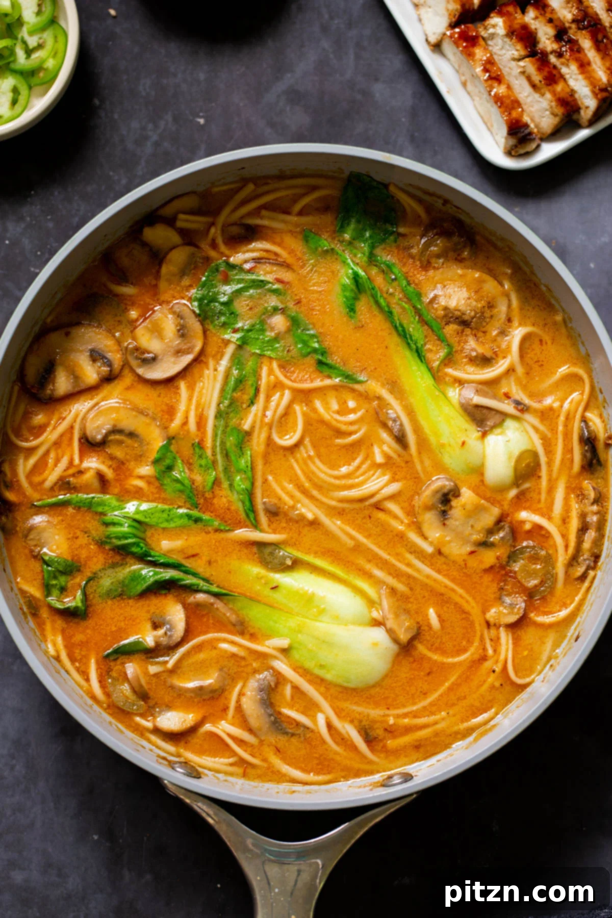 Close-up of a pan of vegan Tonkotsu ramen next to a plate of perfectly seared char siu tofu slices, showcasing the vibrant colors.