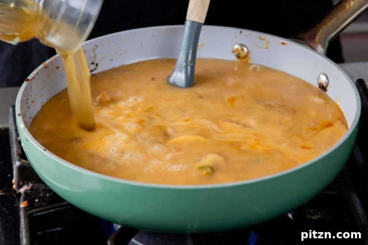 Adding the remaining vegetable broth to the creamy ramen stock in the pan, completing the liquid base for the delicious Tonkotsu.