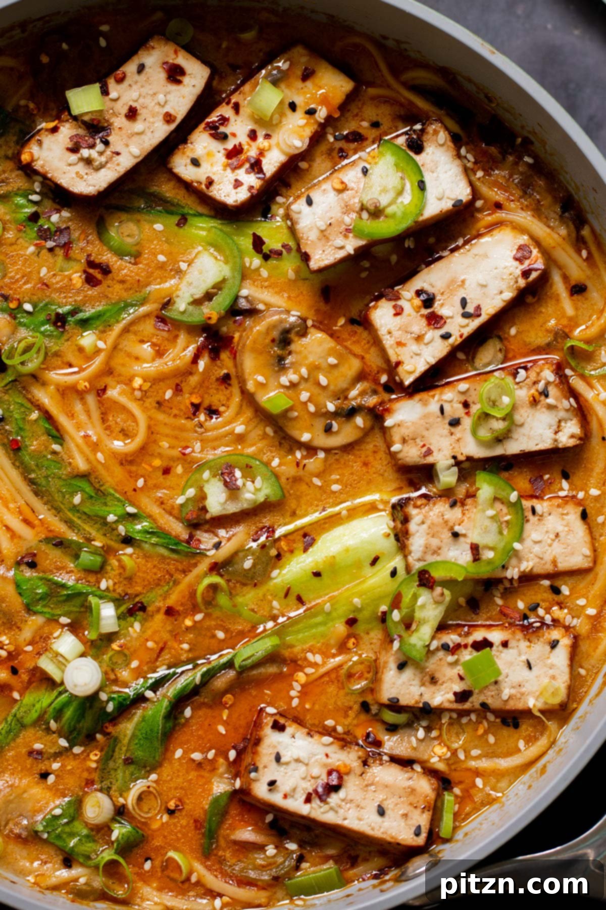 Close-up of the vegan Tonkotsu ramen simmering in a single pot, showing noodles, vibrant bok choy, and creamy broth, with seared tofu slices already added.