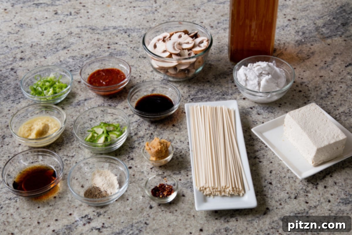 An inviting array of fresh ramen ingredients laid out on a kitchen counter: thin noodles, thinly sliced mushrooms, a container of yellow miso paste, and fresh baby bok choy.