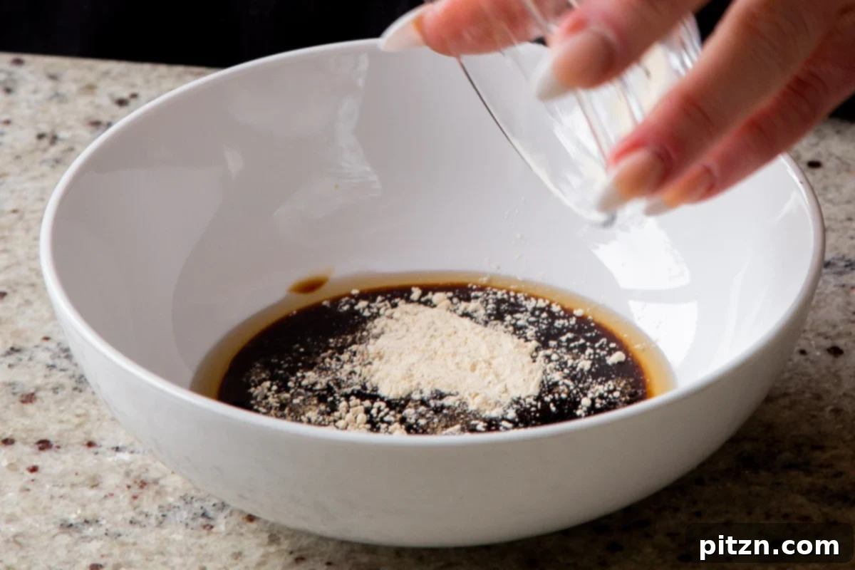 Adding garlic powder to a bowl with other tofu marinade ingredients, including soy sauce, hoisin, and maple syrup, being prepared for the vegan char siu tofu.