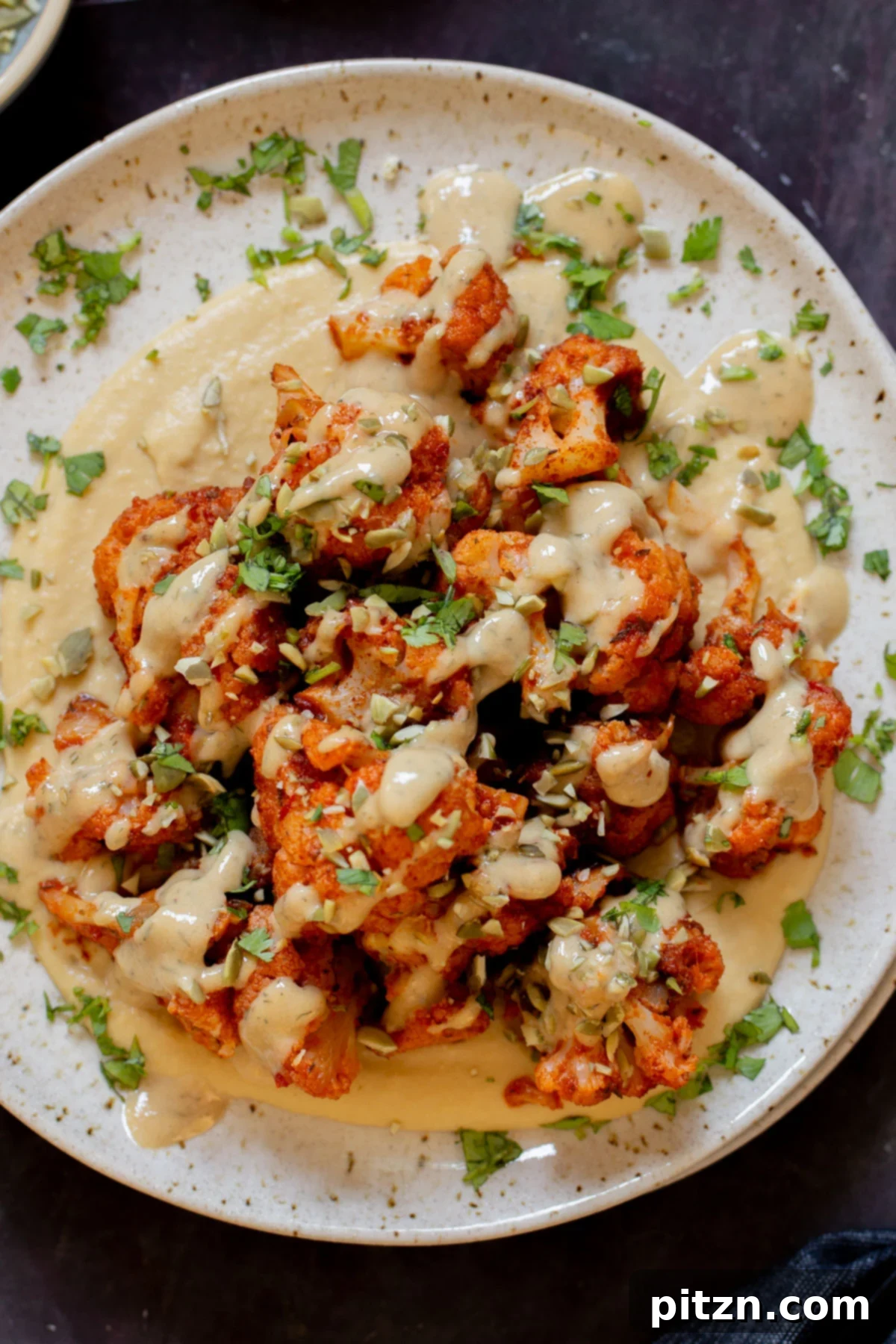 Spicy Harissa Roasted Cauliflower with Creamy Tahini Dill 5 harissa cauliflower on a plate with hummus and tahini dressing, garnished with herbs