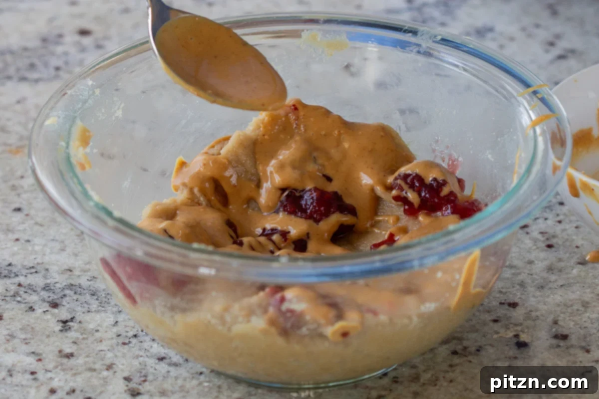 Easy One-Bowl 30-Minute Gluten-Free PB and J Cookies 11 Peanut butter and jelly being artfully added to the almond flour cookie dough for swirling.