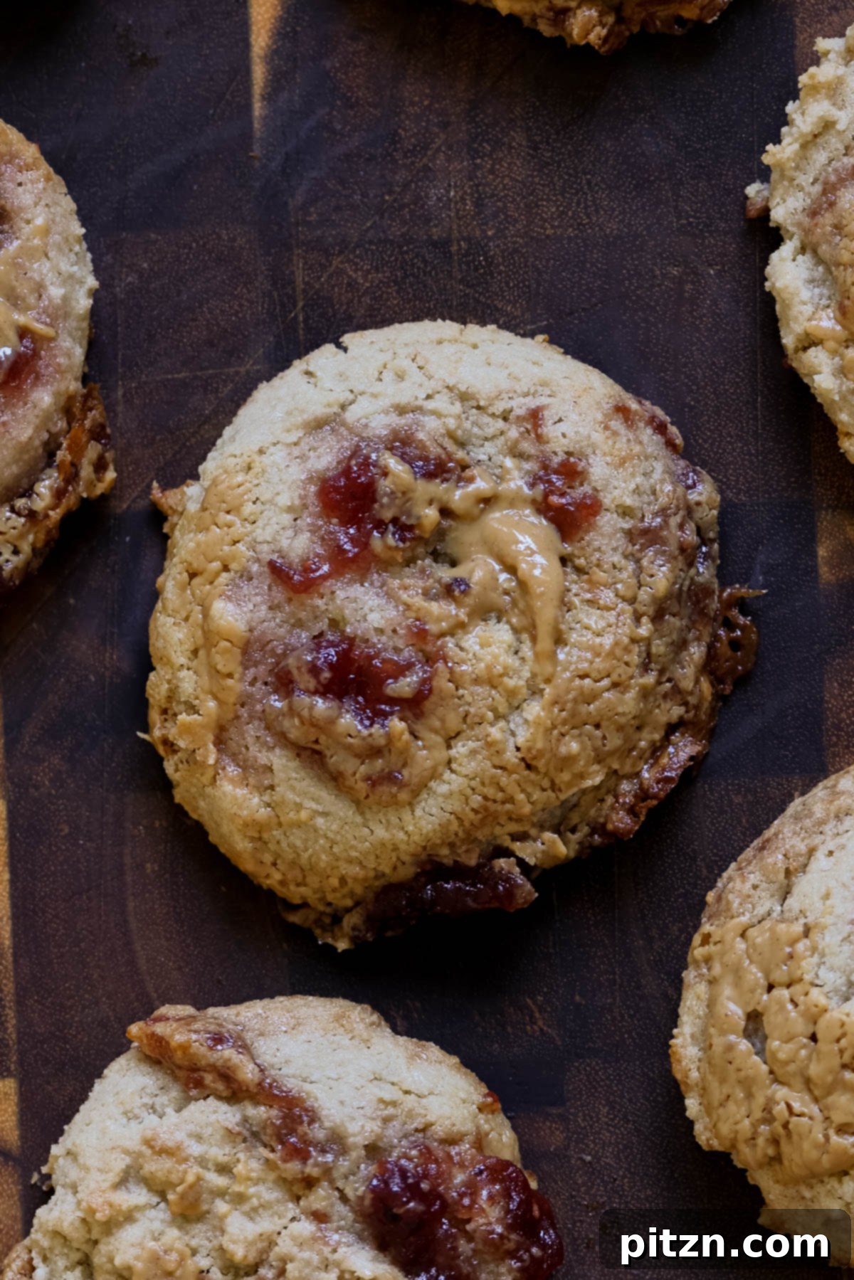 Easy One-Bowl 30-Minute Gluten-Free PB and J Cookies 3 Close-up of gluten-free peanut butter and jelly cookies arranged on a rustic wooden cutting board.