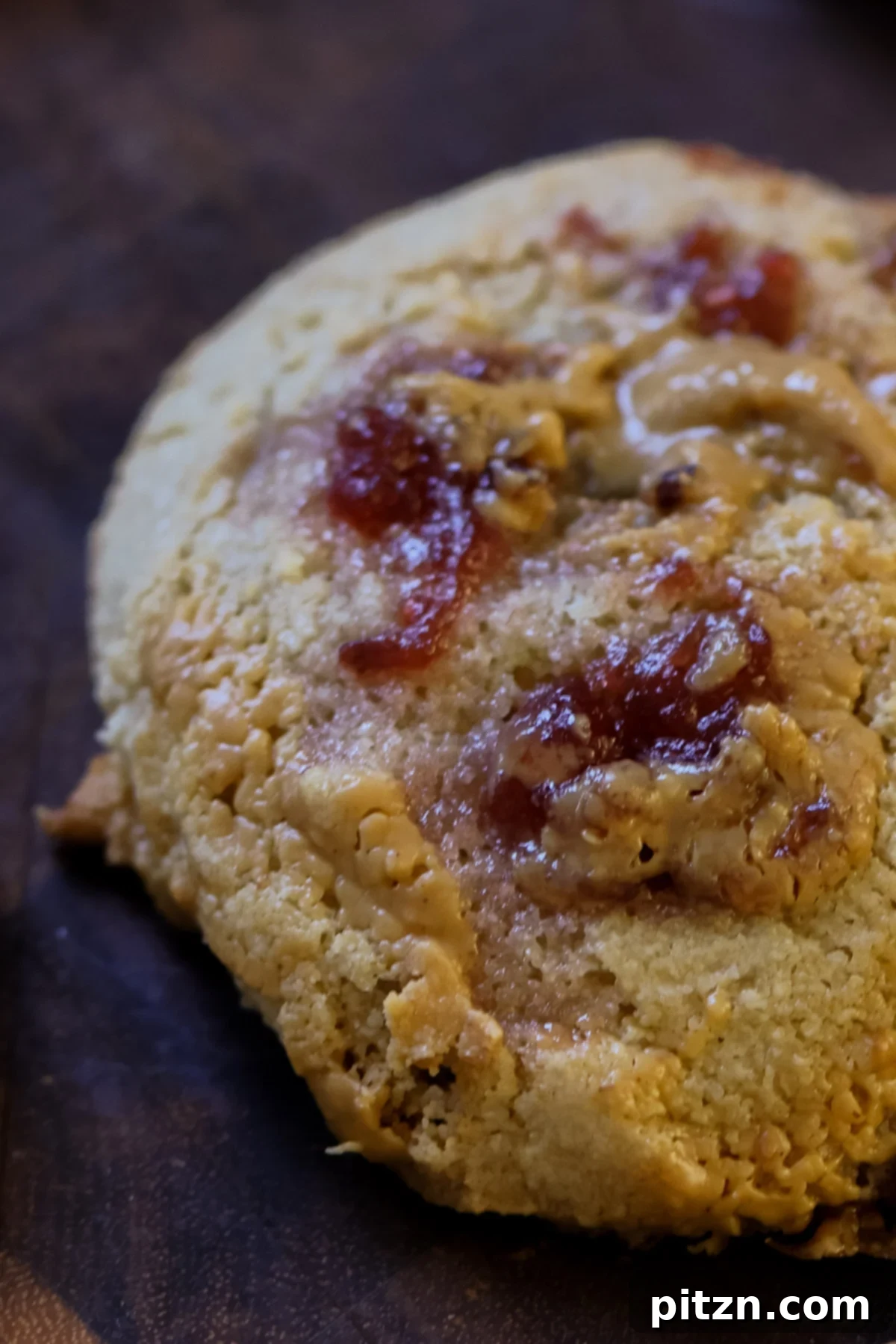 Easy One-Bowl 30-Minute Gluten-Free PB and J Cookies 4 Extreme close-up of a single gluten-free peanut butter and jelly cookie, showcasing its enticing swirls and golden-brown edges.