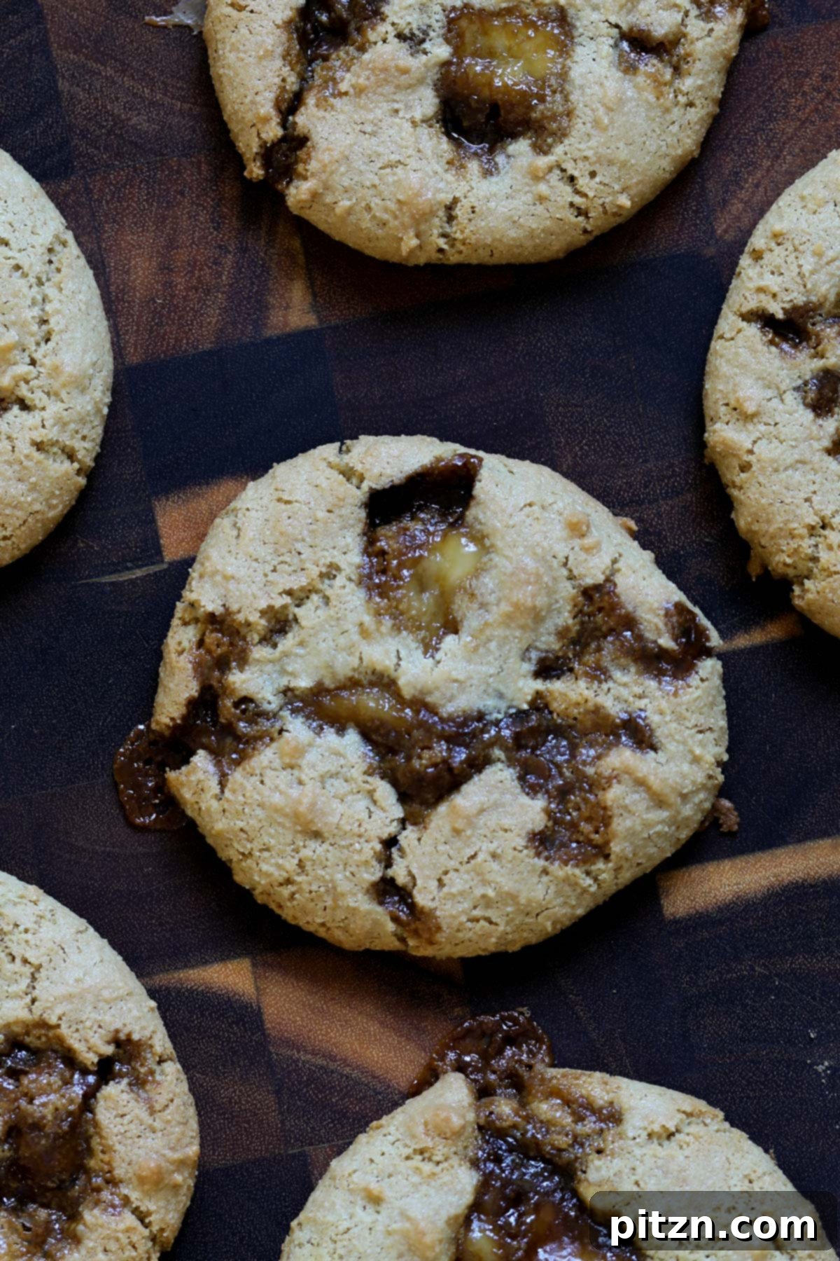 Close-up of a single Tiramisu Cookie showcasing its rich coffee caramel and creamy vegan filling on a rustic wooden board.