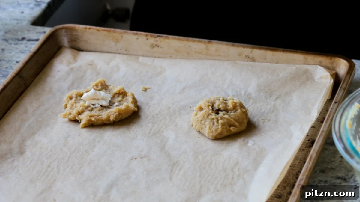 Two unbaked Tiramisu Cookies on a baking sheet: one flattened with cream cheese filling, and another folded over, ready for baking.