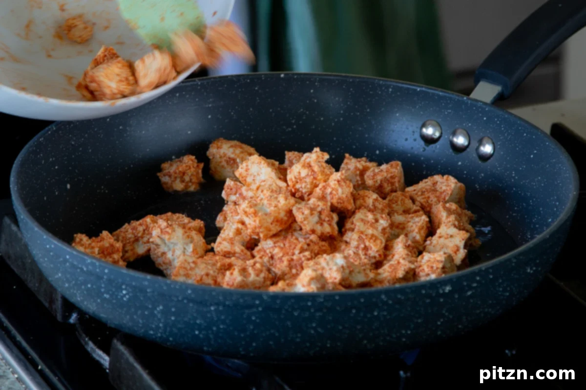 Adding seasoned tofu to a hot pan, beginning the pan-frying process for crispiness.