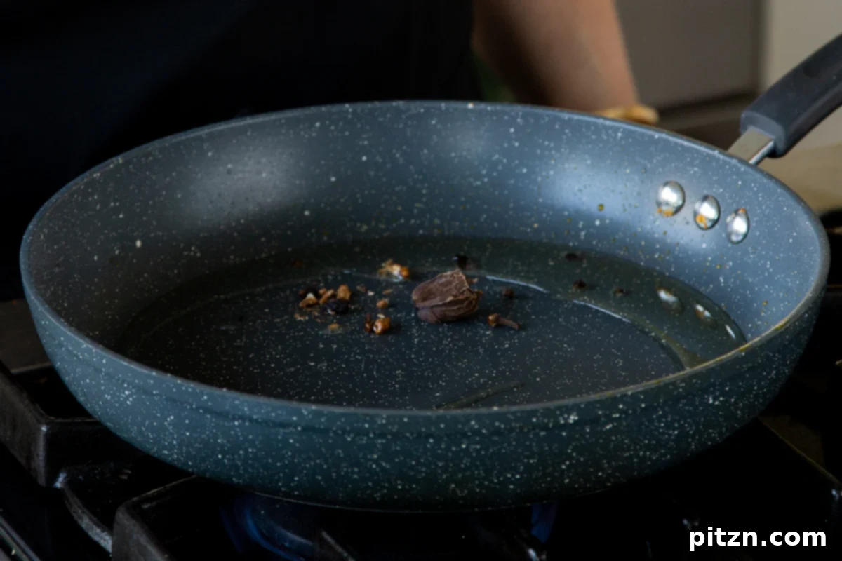 Roasting whole spices in the pan, releasing their aromatic oils and creating the curry's flavor base.