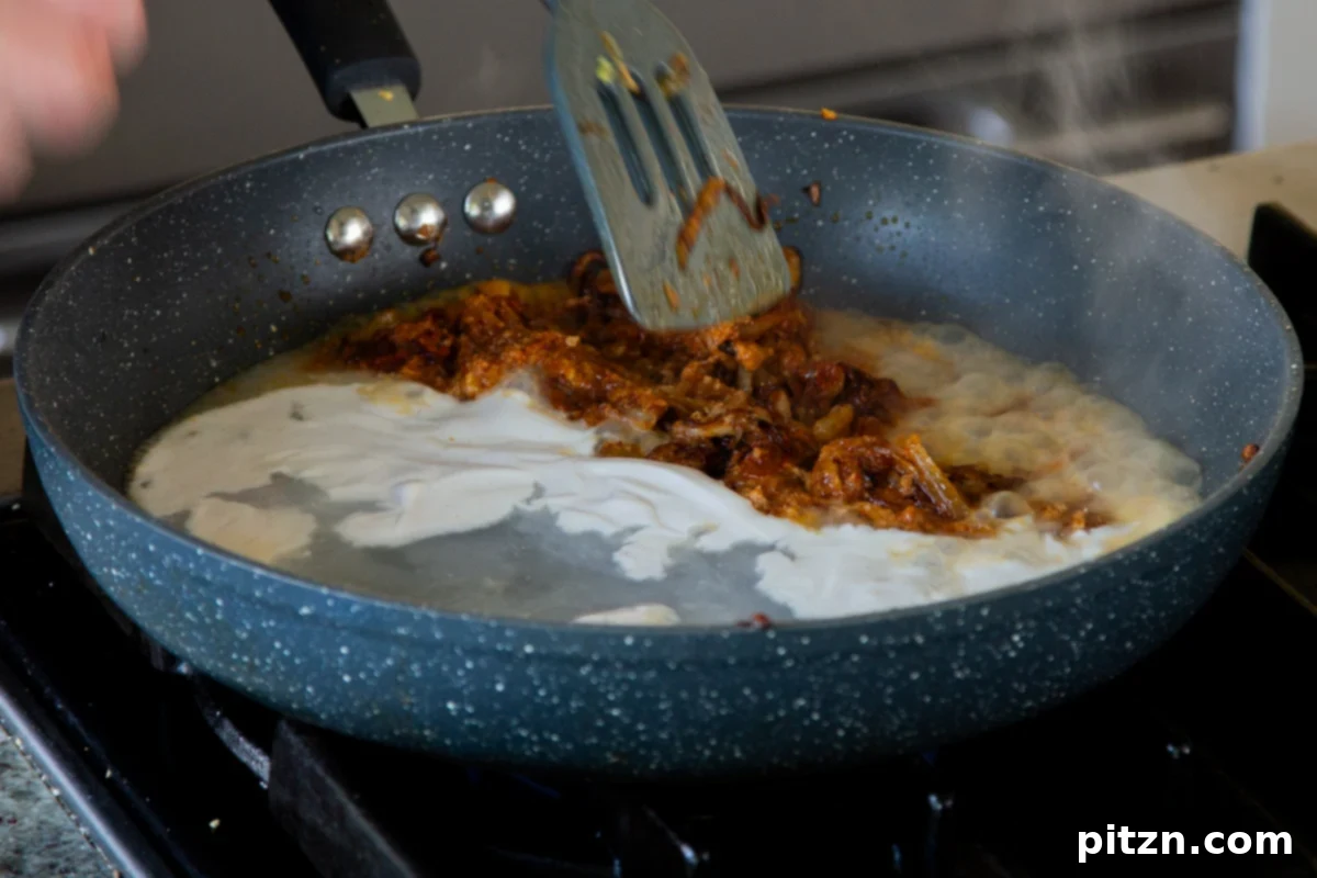 Adding non-dairy yogurt to the onion mixture in the pan, contributing creaminess and tang.