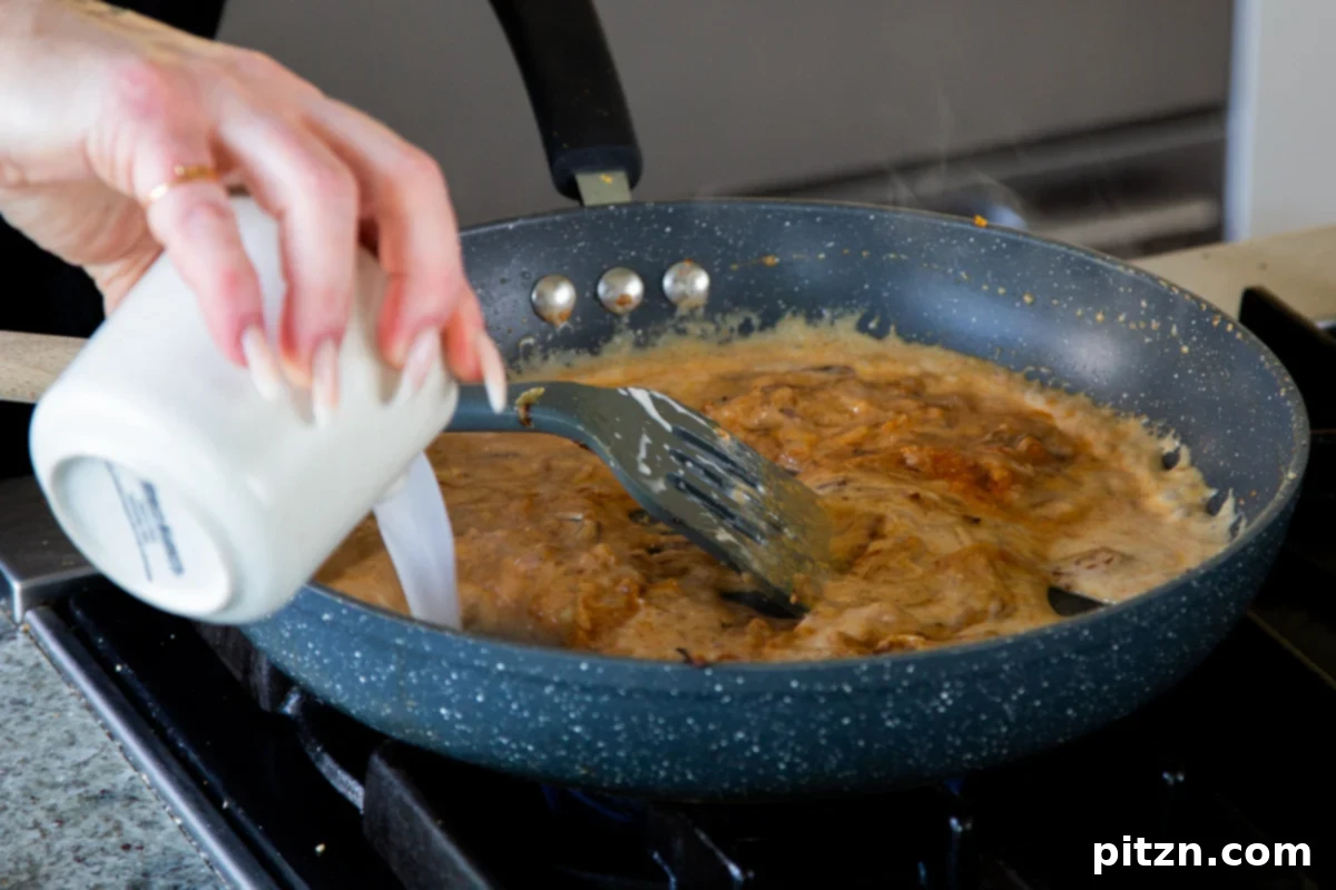 Adding non-dairy milk to the yogurt-onion mixture in the pan, creating a smooth, creamy sauce base.