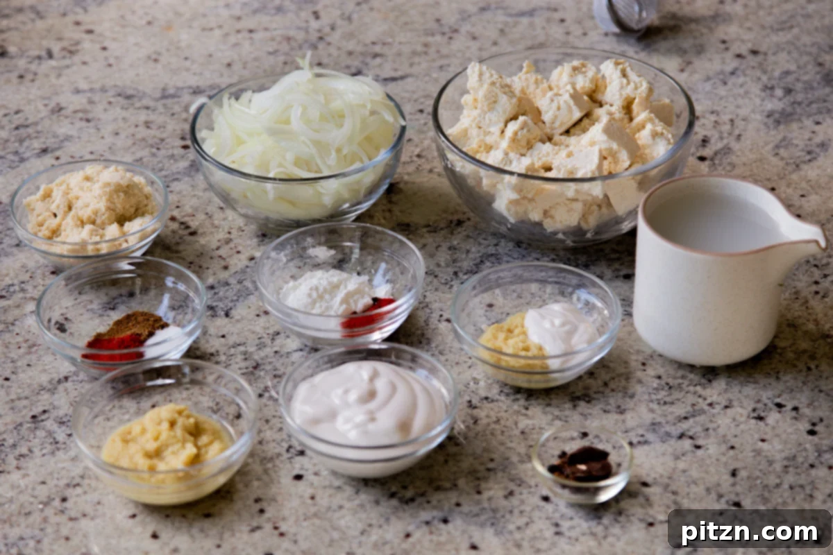 Bowls of tofu, sliced onions, various whole and ground spices, and other ingredients arranged on a kitchen counter, ready for cooking.