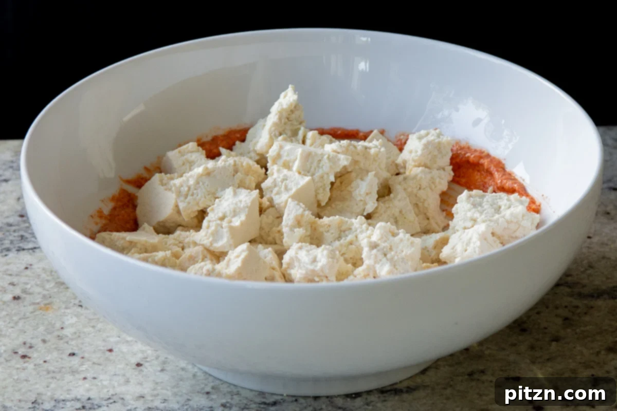 Adding torn tofu pieces to the bowl with the seasoned yogurt mixture, ready for coating.