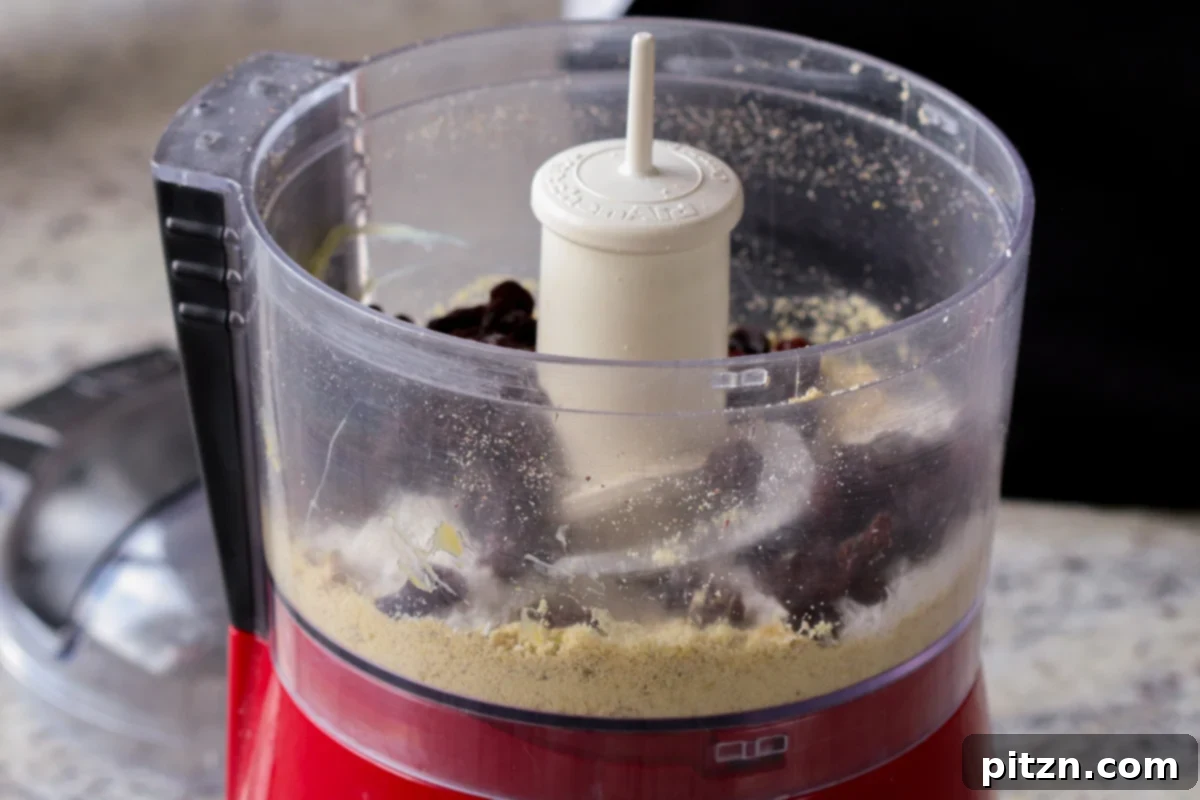 Adding shredded coconut and raisins to the food processor with the ground pistachios to complete the Gujiya filling.
