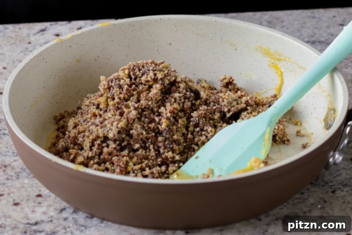 Adding the prepared Gujiya mixture (coconut, pistachios, raisins) to the pan with the remaining custard to bind it.