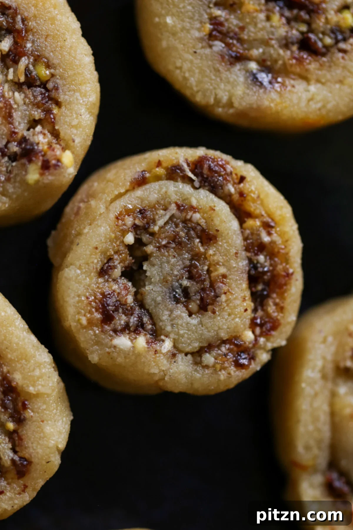 A close-up view of Gujiya Peda on a dark brown plate, highlighting the intricate swirl of the coconut-pistachio filling within the smooth almond fudge.