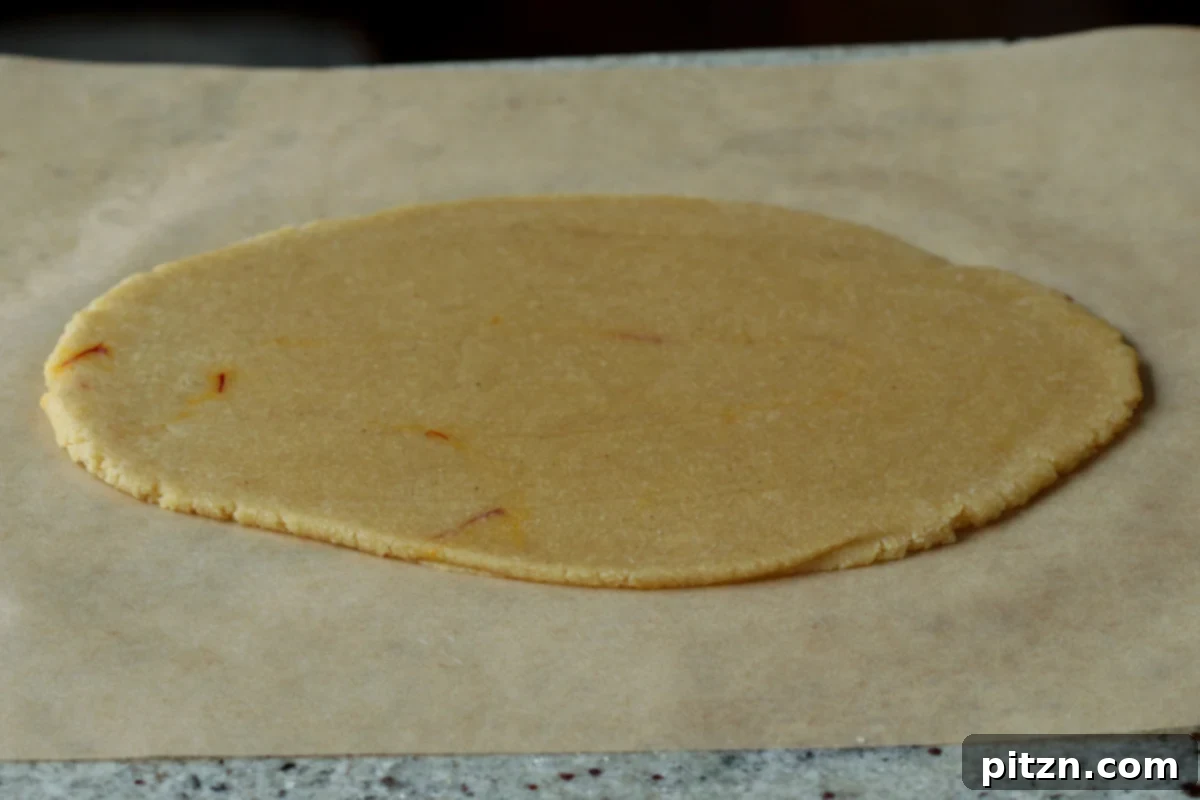 The almond peda dough after being rolled out evenly between parchment paper into a thin rectangle.