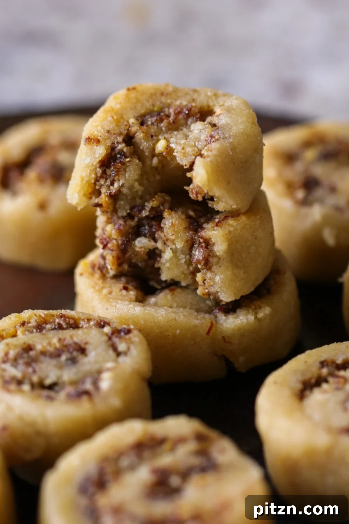 Gujiya Peda pieces stacked, with one bitten into to reveal the beautiful inner swirl of coconut, pistachio, and raisin filling.