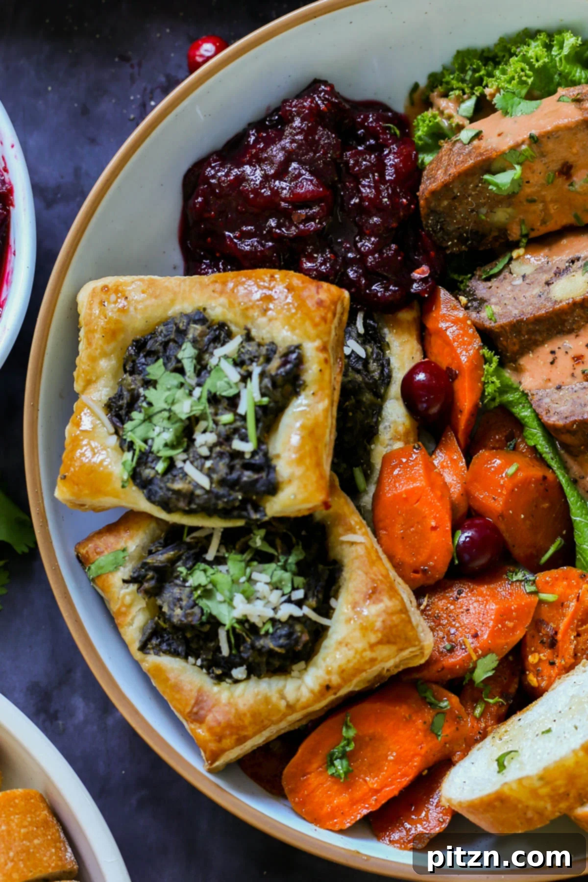 Golden, flaky Indian-spiced spinach puff pastries arranged on a platter with other Thanksgiving dishes, showcasing their vibrant green filling and crispy edges.
