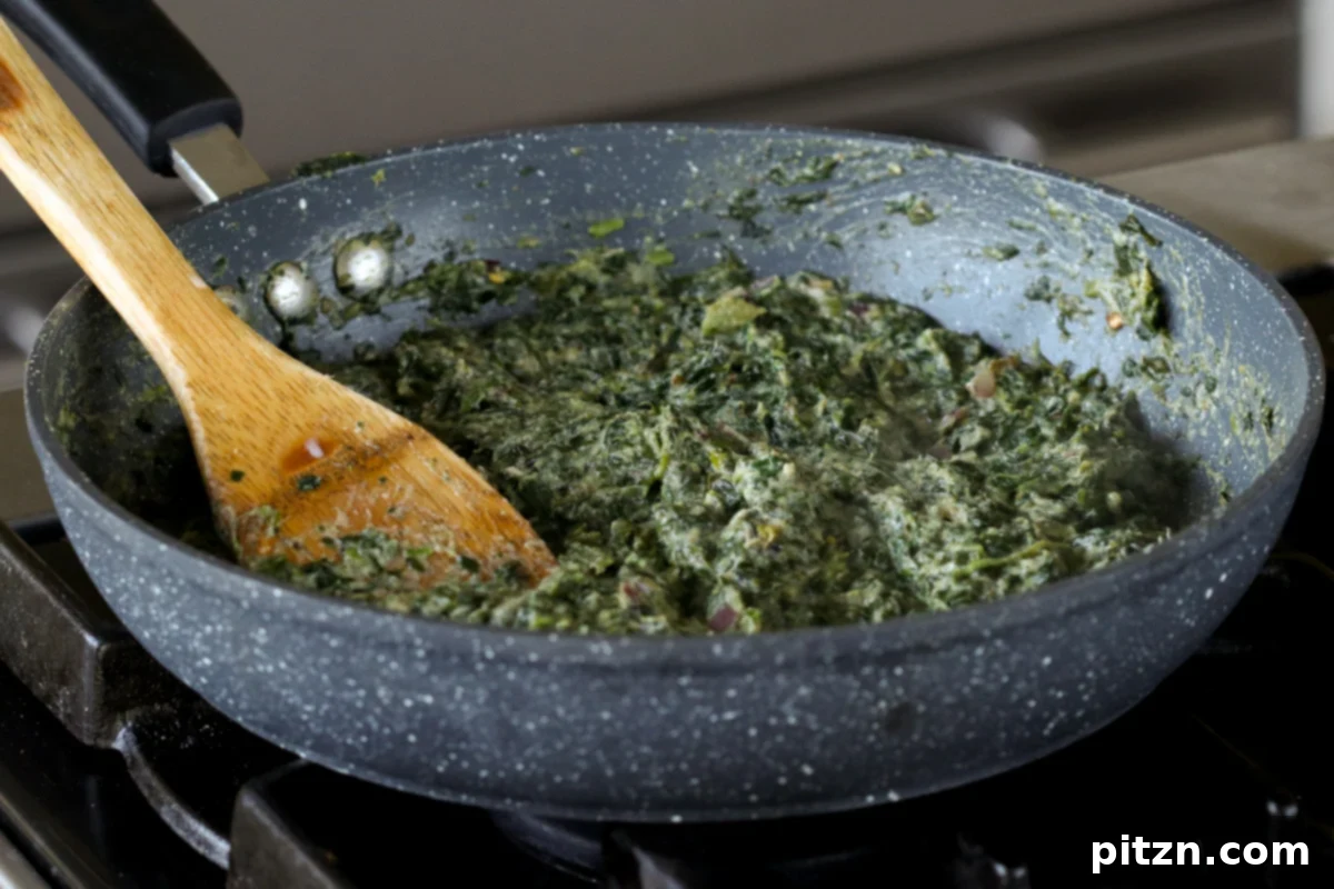 Richly spiced spinach mixture cooking in a pan, showcasing its creamy texture and vibrant green color, ready to be cooled and used for the puff pastry filling.