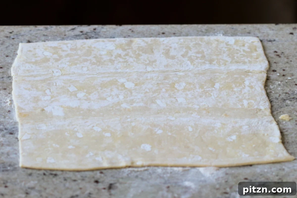 Floured puff pastry sheet on a countertop, expertly rolled and cut into uniform squares, ready for filling and baking.