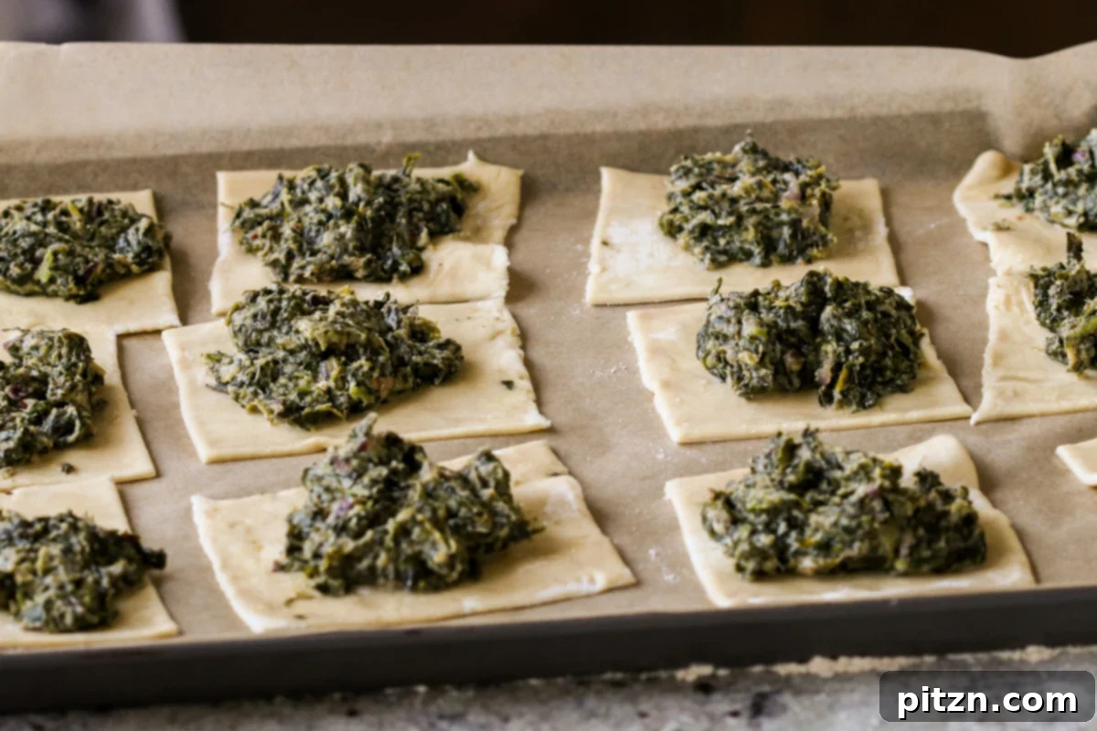 Assembled puff pastry squares with creamy spinach filling meticulously placed in the center, arranged on a baking sheet and ready to be baked to perfection.