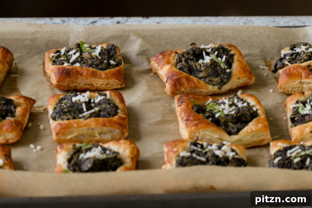 Golden, flaky spinach puff pastries cooling on the baking sheet after being perfectly baked, showcasing their puffed texture and rich filling.