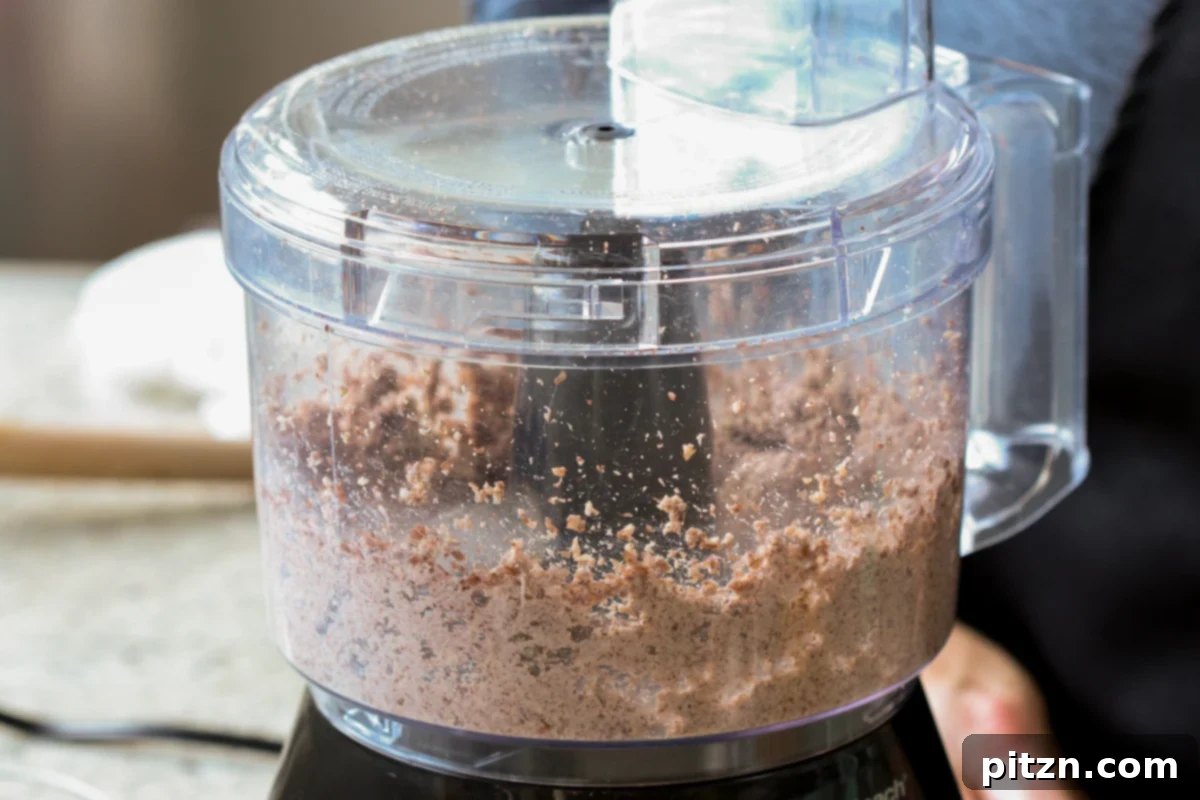 The processed mixture of pecans, chickpeas, and mushrooms inside the food processor, demonstrating the desired coarse texture after initial blending.