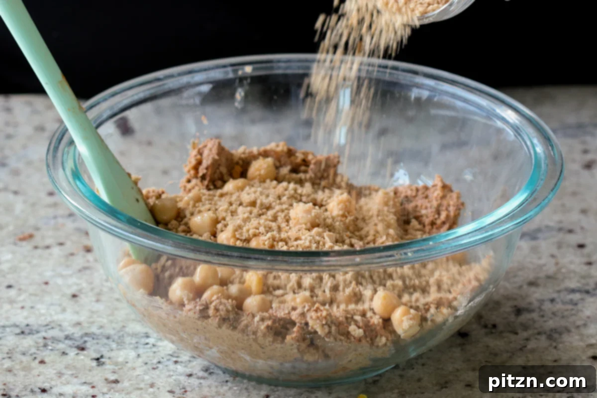 Additional whole chickpeas and breadcrumbs are being mixed into the chickpea loaf dough in a bowl, enhancing texture and binding.