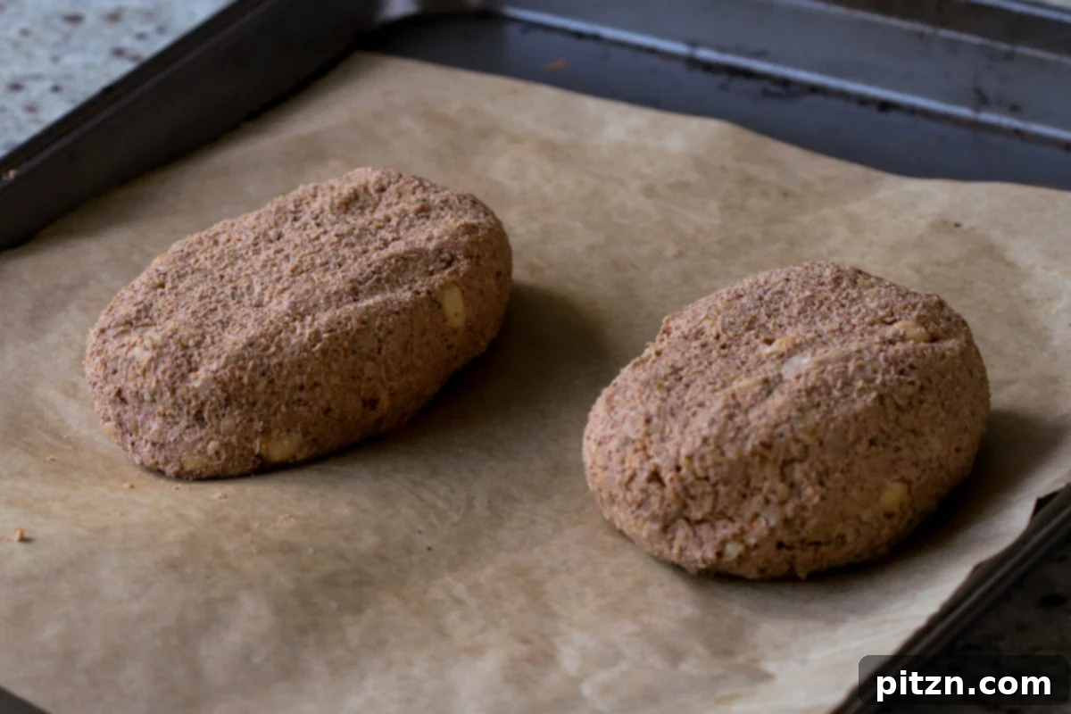 Two perfectly shaped mini chickpea loaves are placed on a parchment-lined baking sheet, prepared for their first round of baking.